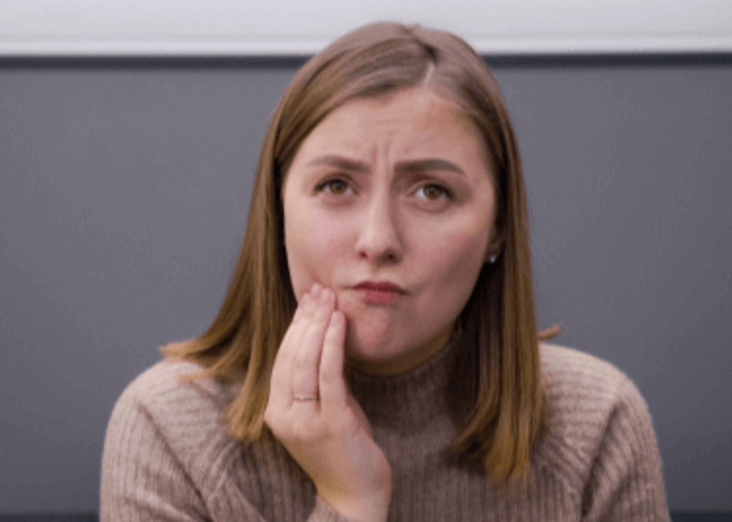 Woman holding onto her cheek as she is in need of an emergency dentist appointment.