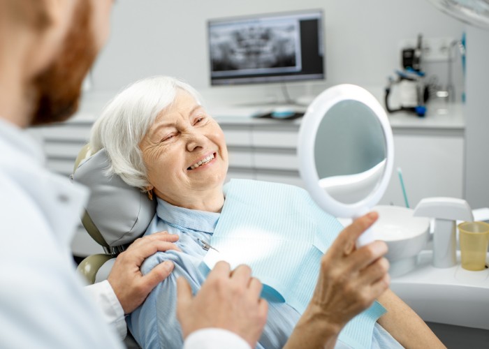 Woman in dentist chair looking in handheld mirror after have tooth loss treated
