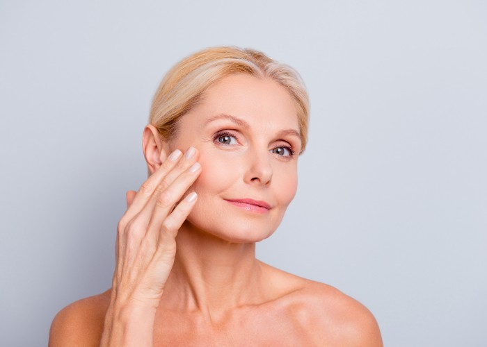 Blonde elderly woman touching her face with anti-wrinkle injection
