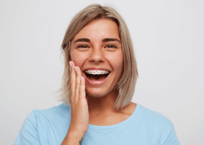 Woman wearing braces holding her face whilst smiling after receiving treatment for her emergency dental issue