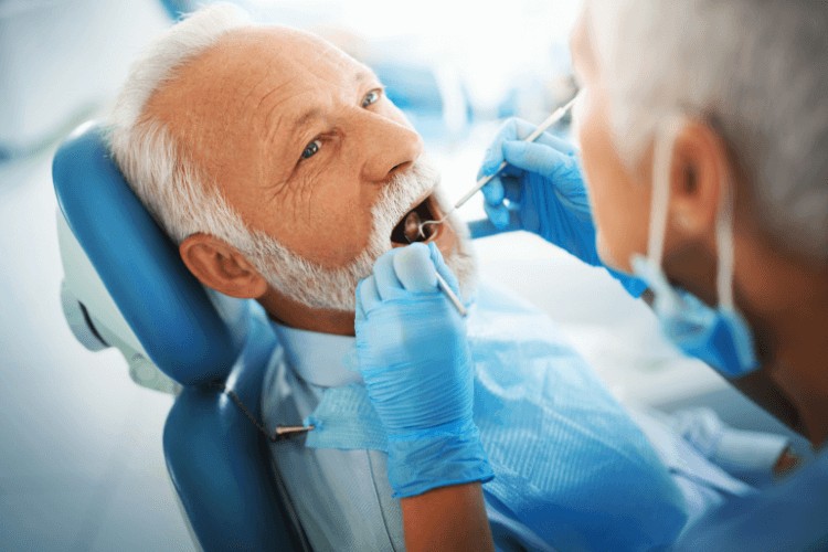 female dentist holding tools checking elderly man’s dental implants