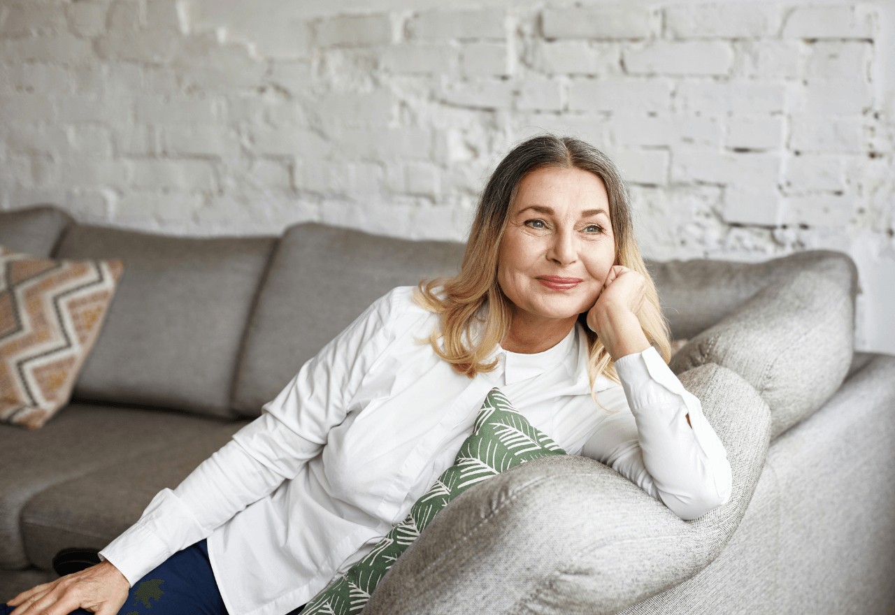 An elder woman smiling away from the camera whilst sitting on a sofa