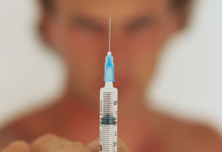 Image of a needle with a blurred mans face in the background.