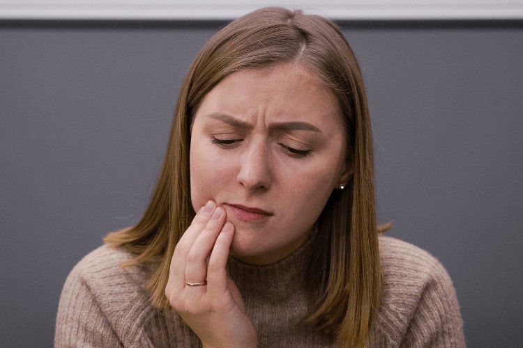 Woman holding her face in pain who has come in for an appointment with one of our emergency dentist at Crescent Lodge Dental Practice.