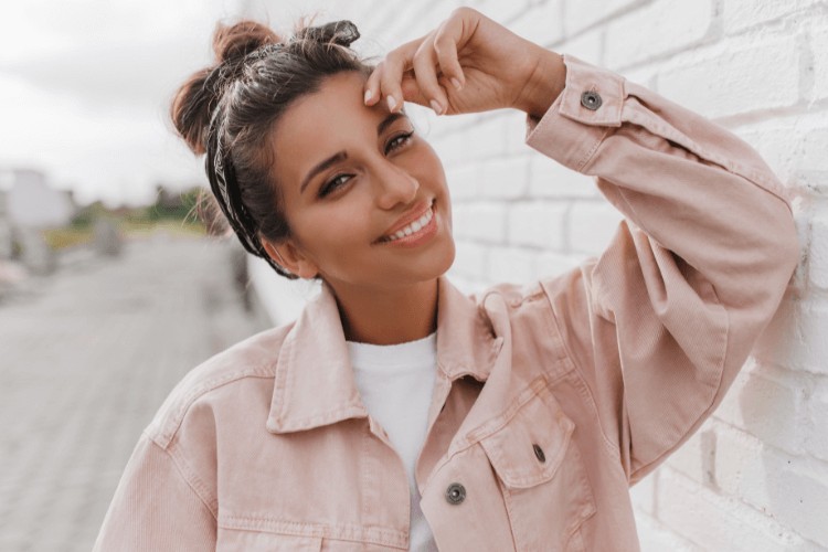 woman in pink jacket touching her head while smiling after white fillings