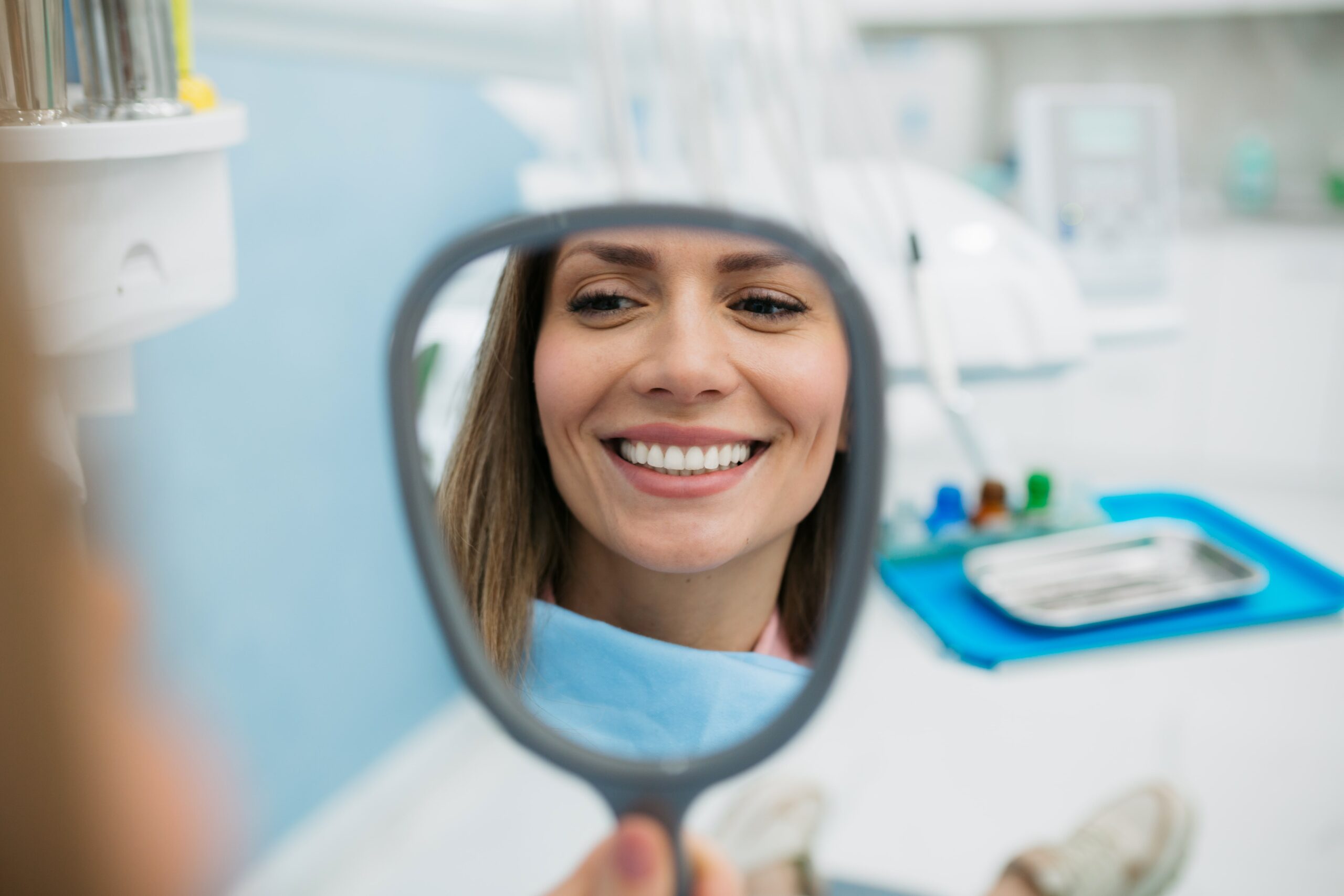 Woman smiling into a mirror at Crescent Lodge Dental Practice, after getting teeth whitening.